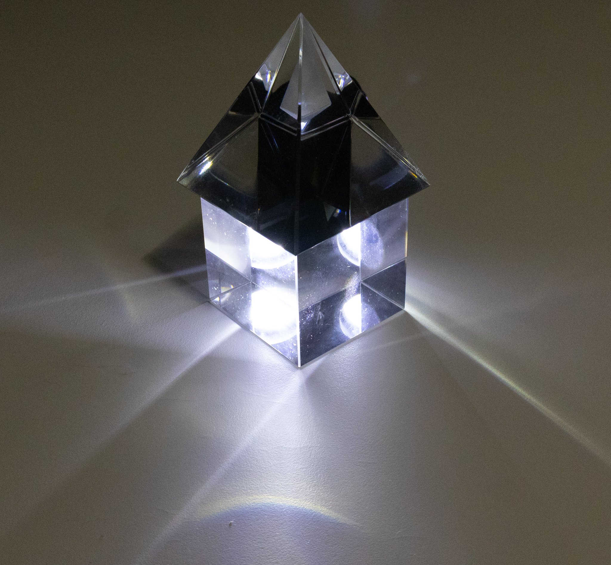 Glass pyramid on top of glass cube, with a light shining behind and through them.